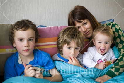 A mother and 3 kids wrapped up on a couch