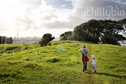 Father and daughter walk across the farm on Mount Hobson volcanic cone, heading toward Auckland City in the distance