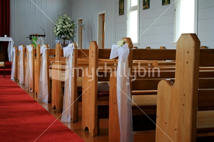 A row of pews in a church, decorated along the aisle with muslin bows and white rose buds for a wedding
