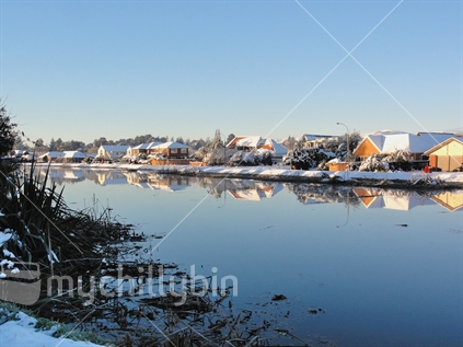 Winter panorama of snow covered houses reflected in the Avon River, Christchurch, South Island, New Zealand.