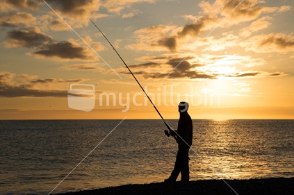 A man fishes in the ocean at sunset
