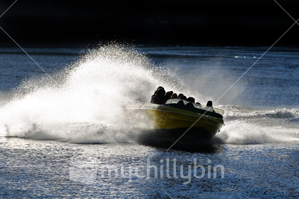 Jet boat with spray from turn in water - back lit
