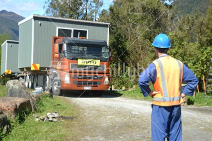 GREYMOUTH, NEW ZEALAND, OCTOBER 21, 2020: A construction worker awaits the arrival of a crane operator who will lift a small transportable building from a truck onto its pilings.