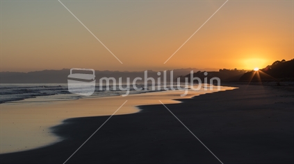 The sunrise reflects on the wet sand of Ohiwa Beach