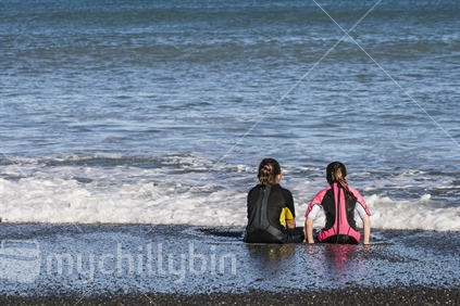 Two young girls in wetsuits waiting for the next wave