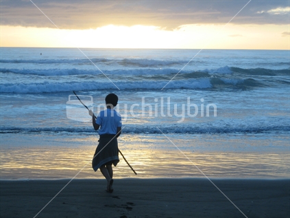 Young boy playing on Bethells Beach at sunset