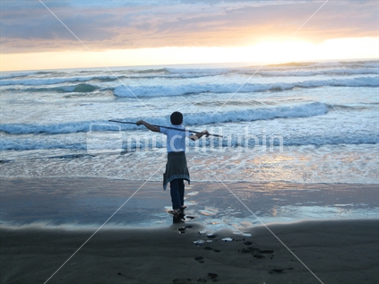 Young boy with stick on Bethells Beach at sunset