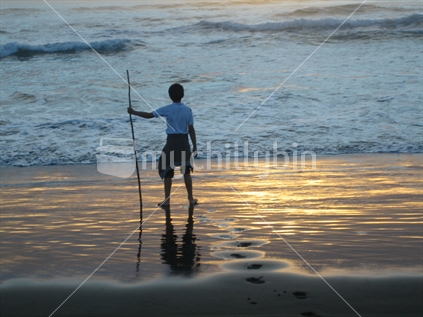 Young boy holding stick contemplating the sunset at Bethells Beach