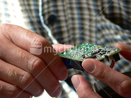 An engineer closely examines a circuit board held in his hands