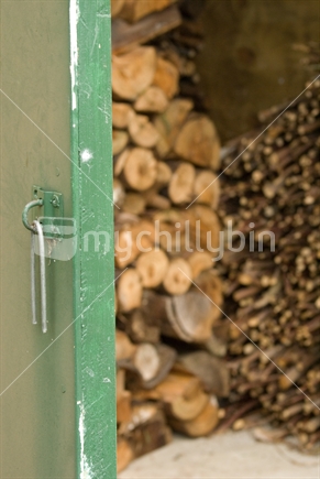 A green woodshed door opens to reveal a stack of firewood