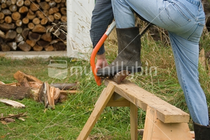 A man works outside cutting up firewood to be put into woodshed
 