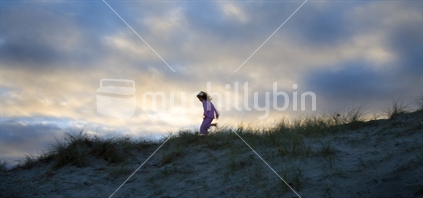 Child running along sand dune at dusk