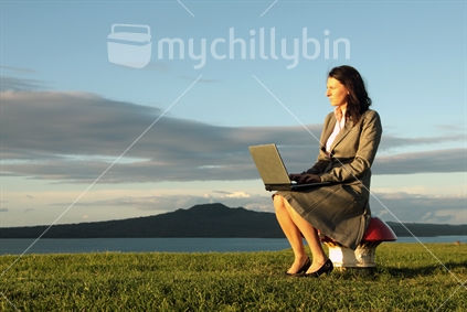 Young business woman working on laptop on Mt. Victoria, Devonport, in evening sun.

