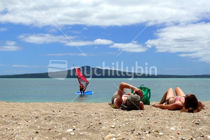 Girls sunbathing on Mission Bay beach with Rangitoto Island and windsurfer