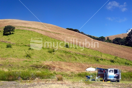 Retro campervan nestled against hill in summertime, New Zealand
