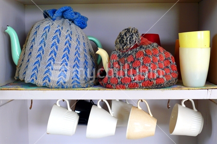 Retro tea pots with tea cosies, plastic cups and hanging cups in bach