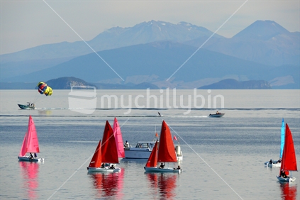 Yachts becalmed on Lake Taupo with waterskier, paraponter and mountains in background, New Zealand