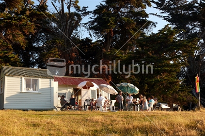 Army hut bach on New Zealand farmland with family gathering at dusk.