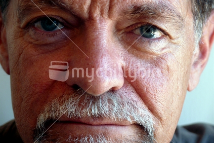 Middle aged man with grey beard and brown tee shirt facing toward the camera, close up