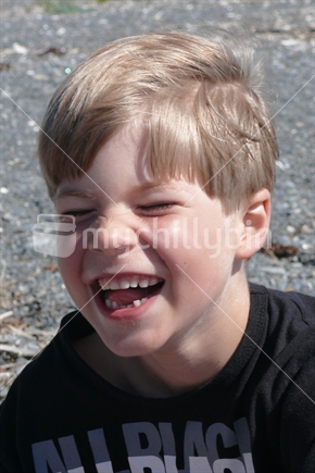 A young boy on a pebbly beach, grinning, showing missing teeth