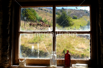 Looking through an old window to vintage farming machinery, with old glass bottles in foreground