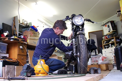 Man working on motorbike at home in man cave (shed).