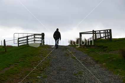 Man walking up farm track, through gates at dusk in winter