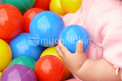 Baby girl's hand around a plastic ball at a birthday party.