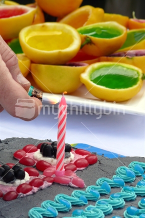One year old's birthday cake candle being lit; with fruit jellies in background