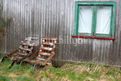 Two old wooden chairs outside wooden home