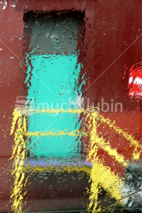 Looking at brightly coloured door with hand rail through rain on the window pane.