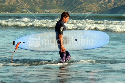 Man heading out to surf at Mahia Peninsular