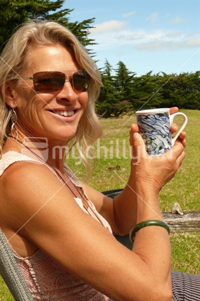 Woman holding a paua shell patterned mug in rural land / park.
