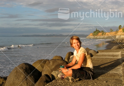 Girl sitiing on beach at sunset with surfers in the background