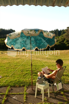 Man with cup of tea sitting under retro sun umbrella at sunset