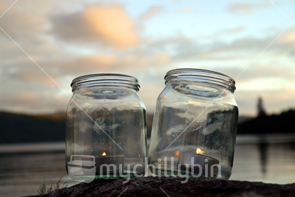 Glass jars with tea light candles beside lake