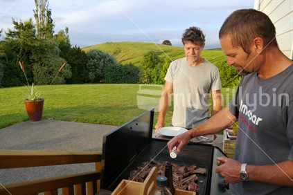 Two men barbequeing chops on rural property