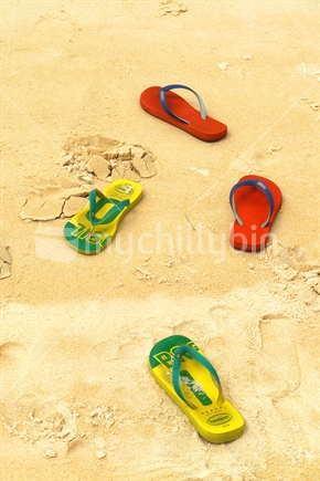 Two pairs of jandals left on golden sand (Note USA Havaianas brand details show). 