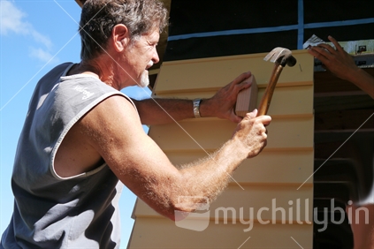 Builder hammering in cladding on renovated house