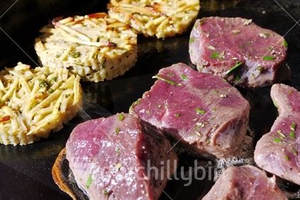Venison steaks and potato patties cooking on a barbeque