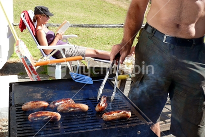 Girl reading a book while father barbeques