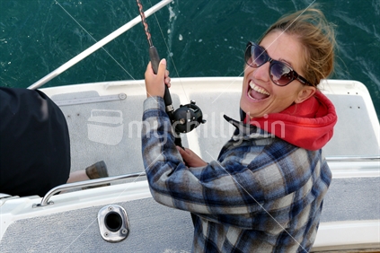 Young woman fishing for trout on the back of a boat, on Lake Taupo