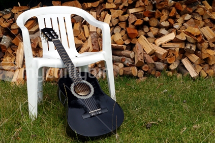 Guitar resting against plastic picnic chair with stacked firewood behind