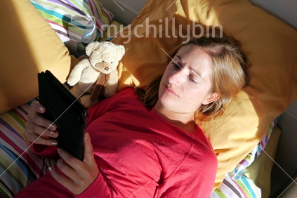 Young woman lying in the afternoon sun, reading an electronic book