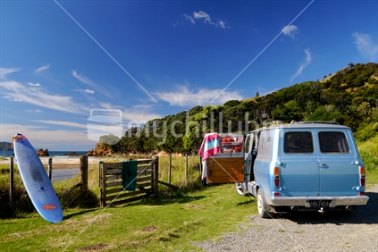 Retro campervan parked at end of beach road with beach towel and surfboard