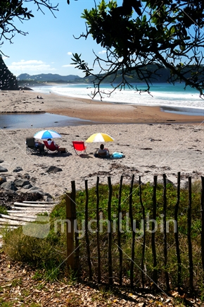 A couple sitting under bright coloured beach umbrellas, Hot Water Beach, The Coromandel
