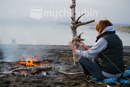 Woman warming herself by a campfire