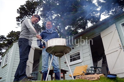 Two middle aged men barbequing on wood barbeque