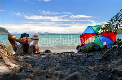 Man relaxing on shores of Lake Taupo with retro sun umbrella and thermos flask