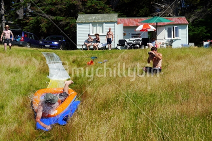 Man water sliding down hill with army hut bach and onlookers